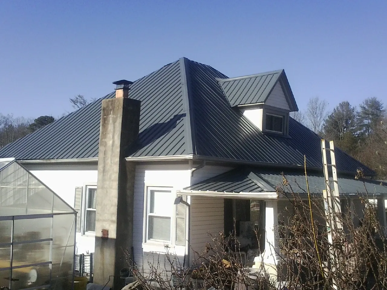 Dark blue standing seam metal roof on a white farmhouse with dormer — Slate & Tile Roof Repair by Roofing Brothers in South Haven